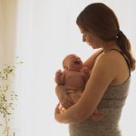 Young unemotional mother holding crying newborn in her arms. Woman in postpartum depression has no strenght to calm down her crying baby. Lonely exhausted mother at home.