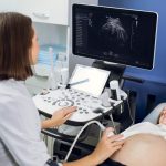 Happy pregnancy time, ultrasound concept. Pretty pregnant woman doing ultrasound scan in the prenatal clinic, worried about health of her future baby. Female doctor looking at the screen.